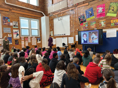 Crowded room of kids sitting on ground listening to teacher